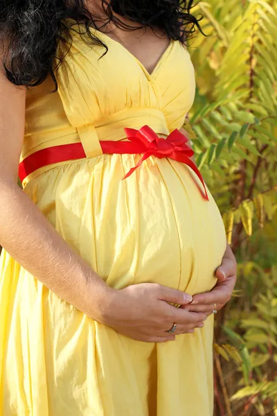 Zblízka břicho těhotné ženy ve žlutých šatech — Stock fotografie