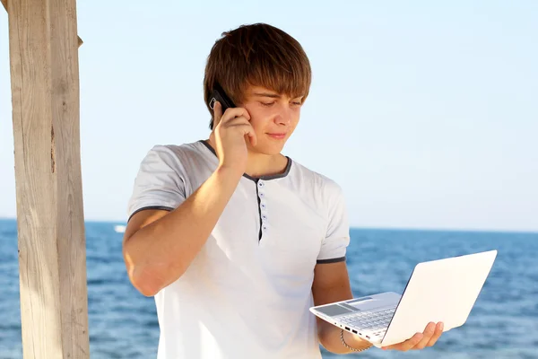 Ung man med mobiltelefon med laptop på stranden — Stockfoto