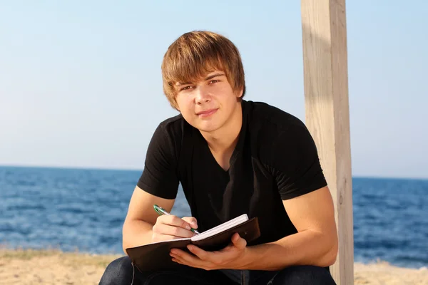 Jovem atraente com almofada de escrita na praia — Fotografia de Stock
