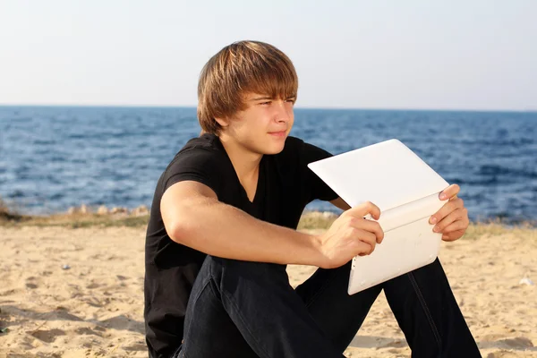Мыслящий парень с ноутбуком, отводящий взгляд на пляже — стоковое фото