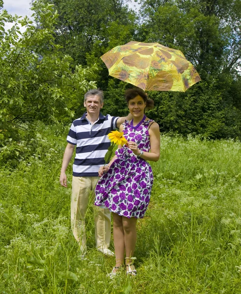 Young man and woman with sunflower and yellow umbrella — Stock Photo, Image