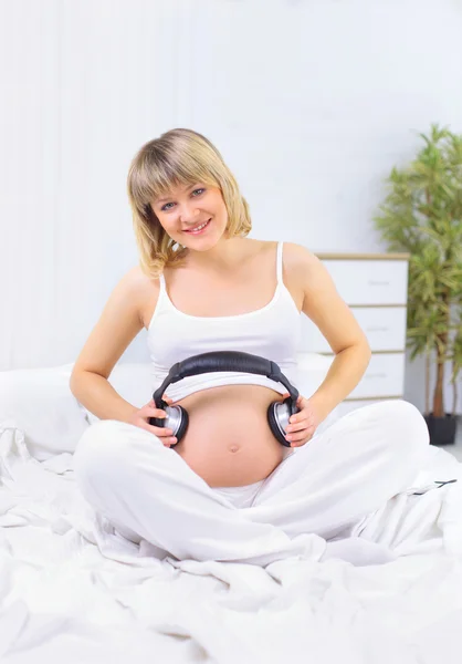 怀孕的女人在家里白色沙发上坐着聆听音乐 — 图库照片