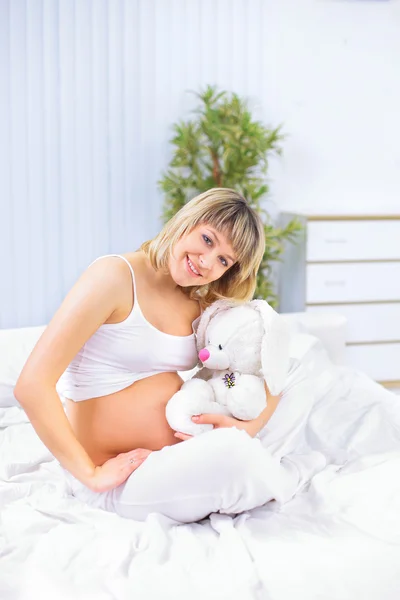 Mujer embarazada con peluche sentado en el sofá blanco en casa —  Fotos de Stock