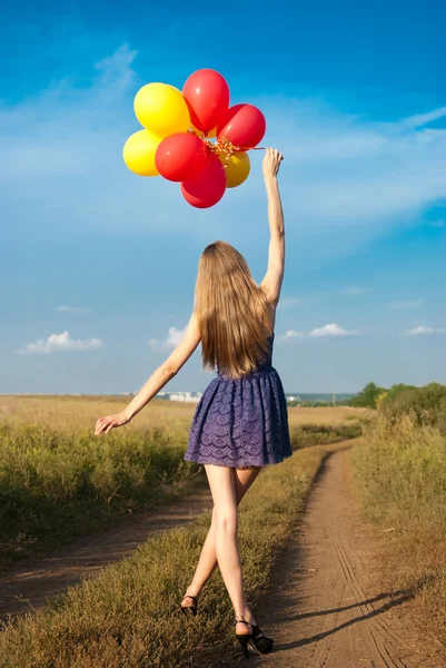 Menina em vestido curto andando ao longo de uma estrada rural com os balões em seu h — Fotografia de Stock