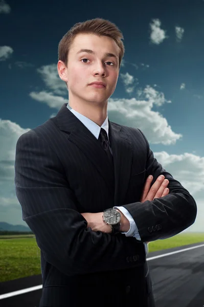 背景の青い空の雲にスーツで自信を持って若いビジネスマン — ストック写真