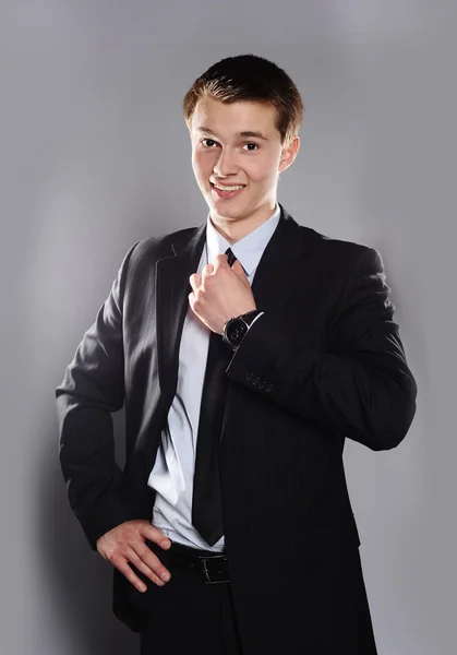 Mladý podnikatel s úsměvem a narovnává kravatu izolován v šedé — Stock fotografie