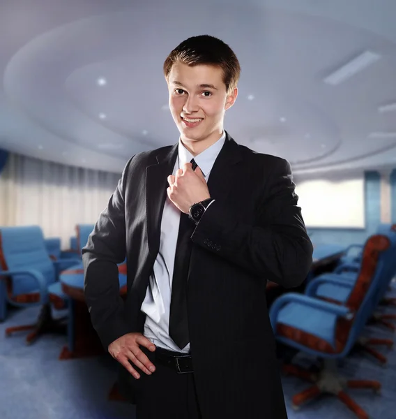Smiling young businessman adjusts his tie in the office — Stock Photo, Image