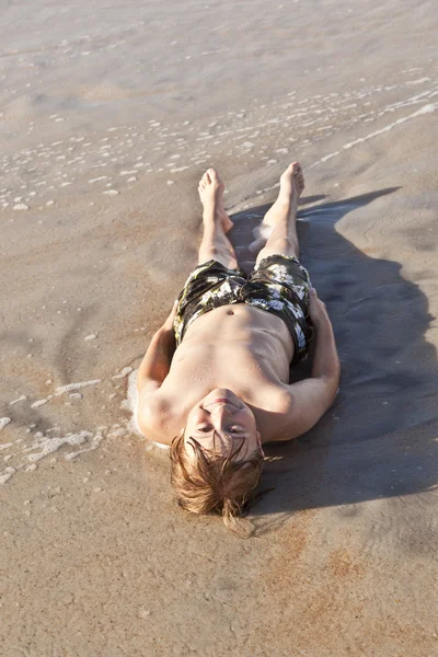 少年はビーチで横になっていると、太陽を楽しむ — ストック写真
