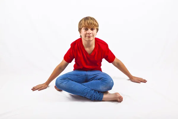 Chico inteligente con camisa roja sentado en el asiento del sastre en el suelo —  Fotos de Stock
