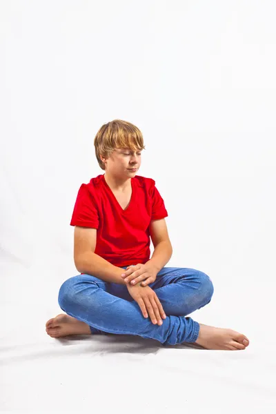 Умный мальчик в красной рубашке, сидящий в кресле портного на полу — стоковое фото