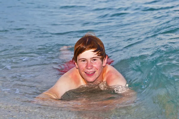 少年はビーチで横になっている、海の波を楽しんでいます — ストック写真