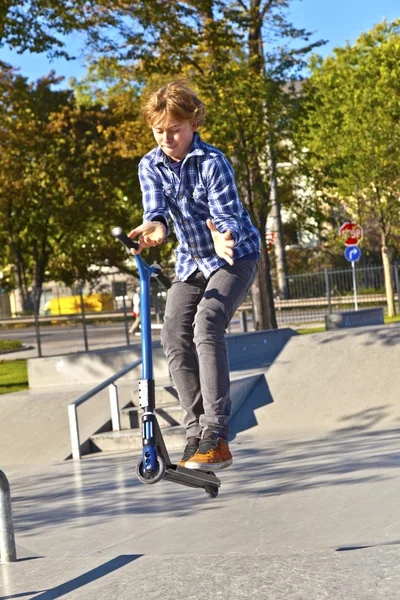 Pojken hoppar med sin skoter på skateboardpark — Stockfoto