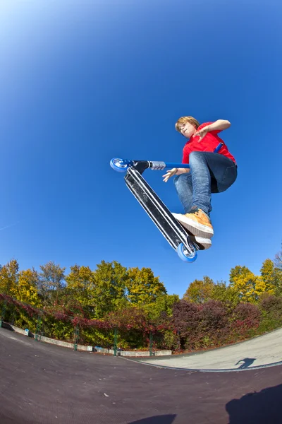 Chłopiec, skoki z jego skuter w skate parku w jasny niebieski — Zdjęcie stockowe