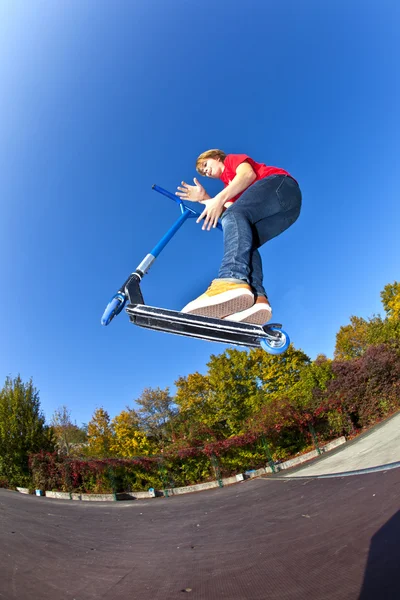 Garçon sautant avec son scooter au skate park sous bleu clair — Photo