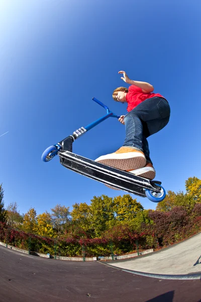 Boy jumping with his scooter at the skate park under blue clear — Stock Photo, Image