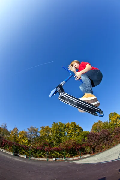 Chłopiec, skoki z jego skuter w skate parku w jasny niebieski — Zdjęcie stockowe
