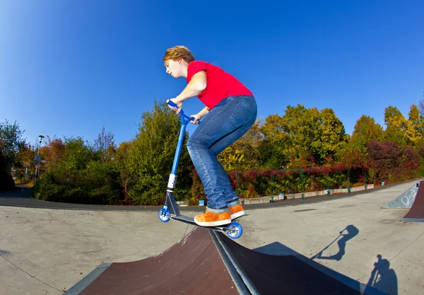 Niño saltando con su scooter en el parque de skate bajo azul claro — Foto de Stock