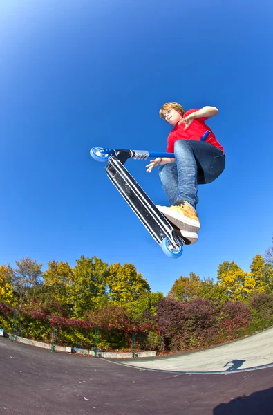 Boy jumping with his scooter at the skate park under blue clear — Stock Photo, Image