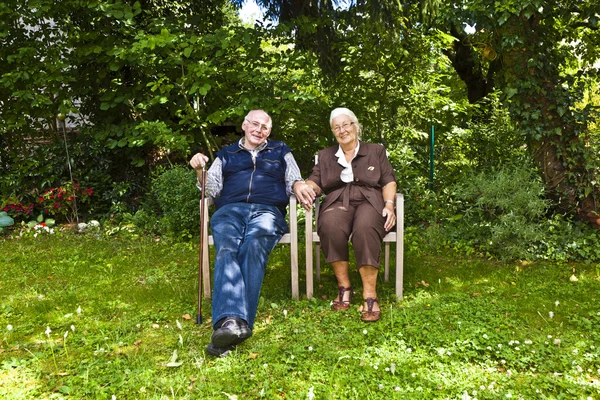 Anziani coppia seduta mano nella mano nel loro giardino — Foto Stock