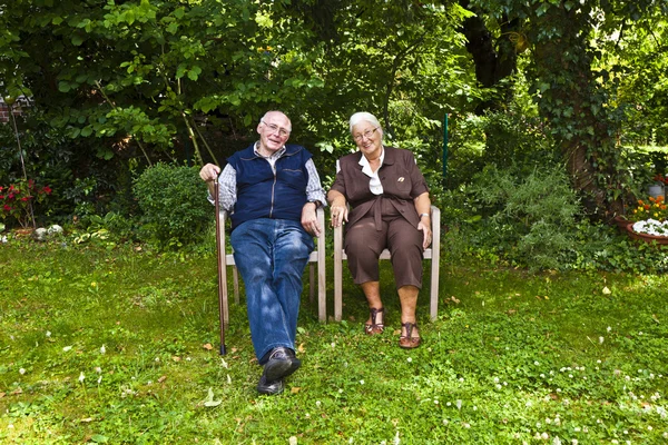 Elderly couple sitting hand in hand in their garden — Stock Photo, Image