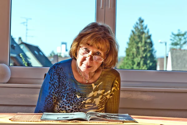 Ältere attraktive Frau liest zu Hause in einer Zeitschrift — Stockfoto