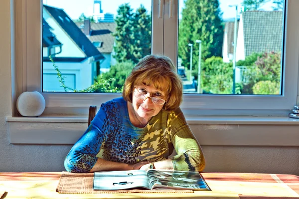 Ältere attraktive Frau liest zu Hause in einer Zeitschrift — Stockfoto