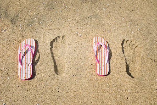 Sandalen und Fußabdrücke im Sand — Stockfoto