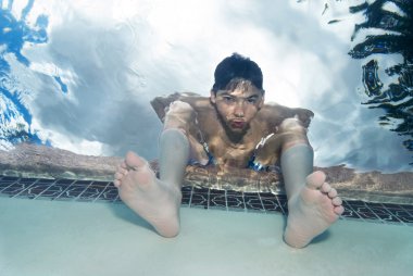 Boy sitting at swimming pool edge clipart