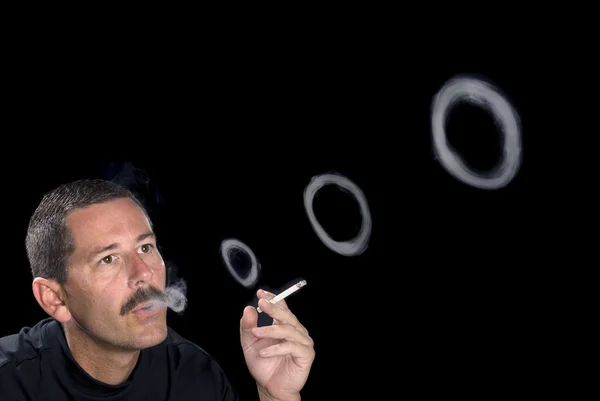 Человек курит и выдувает дымовые кольца — стоковое фото