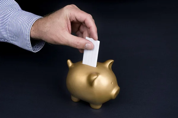 Putting slip of paper in piggy bank — Stock Photo, Image