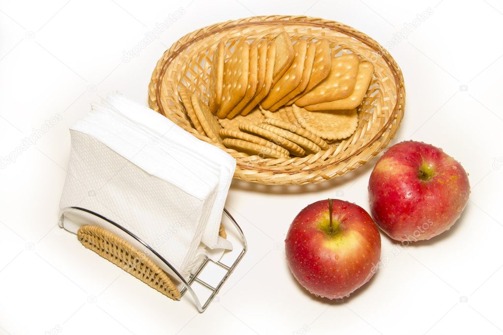Two red apples, napkin holder, wicker plate with cookies