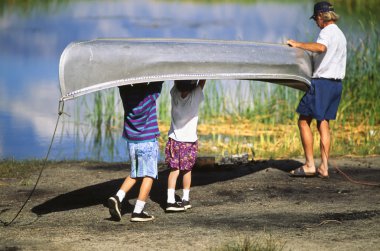 Father and sons carry a canoe to the lake. clipart