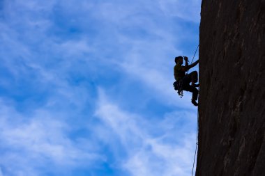 Rock climber clinging to a cliff. clipart