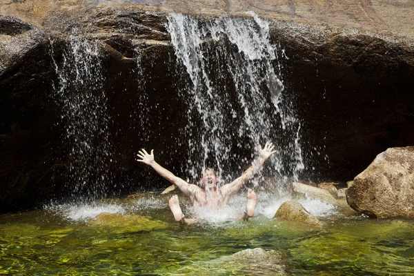Muž slaví pod vodopádem. — Stock fotografie