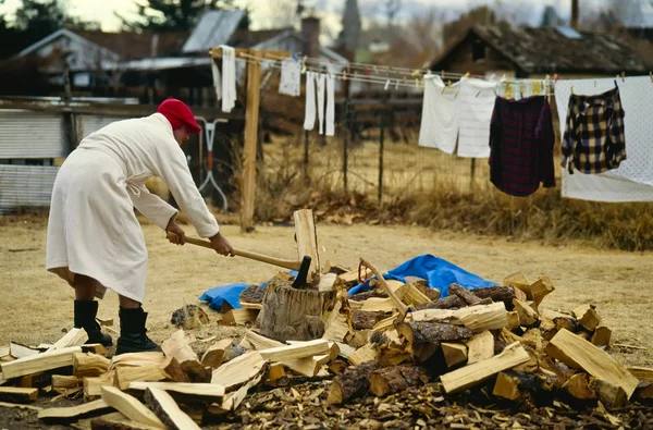 Mann im Mantel hackt Brennholz. — Stockfoto