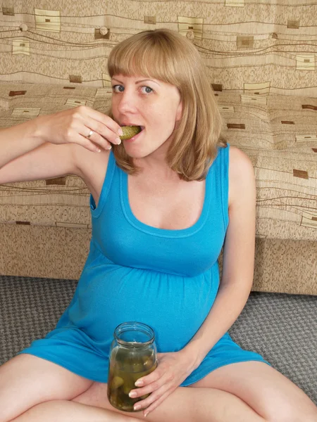 A mulher grávida come um escabeche, sentado em um soalho — Fotografia de Stock