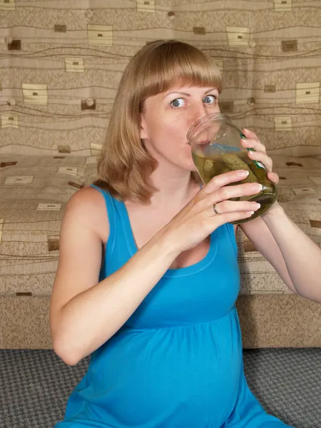 De zwangere vrouw drinkt een pekel, zittend op een vloer — Stockfoto
