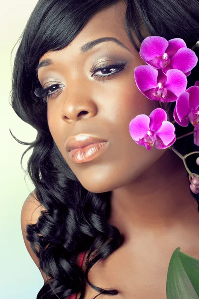 Hermosa cara de mujer joven con flores de orquídea púrpura — Foto de Stock
