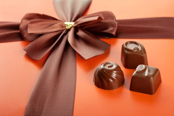Milk chocolates and beautiful gift box with ribbon bow, closeup — Stock Photo, Image
