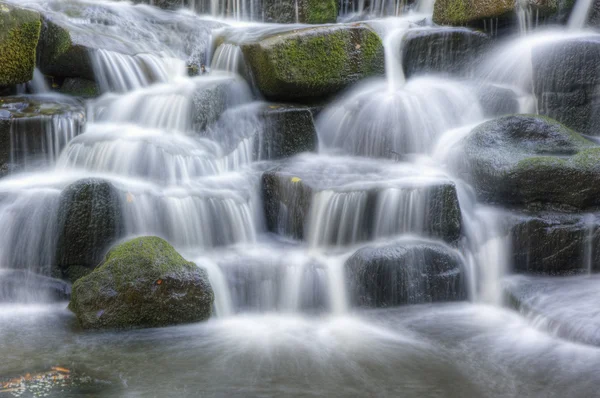 漂亮的瀑布瀑布一样流到岩石在郁郁葱葱的森林景观 — 图库照片