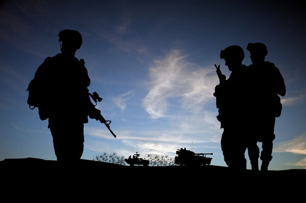 Силуэт современных солдат на фоне заката с военными в руках

