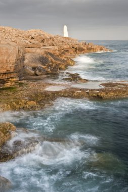 Stunning geological rock cliff formations with waves crashing in clipart