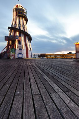 Helter skelter fun fair ride on pier at sunset clipart