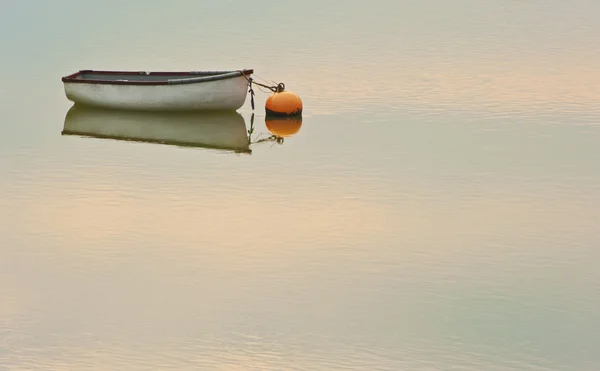 Barco a remo solitário e bóia no mar com pôr do sol refletida em ri — Fotografia de Stock