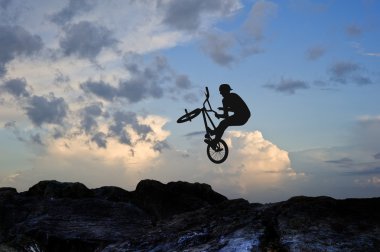 Silhouette of bmx bike doing trick against beautiful sky clipart