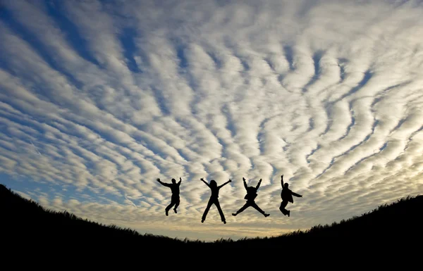 Silhhuette of four adults jumping for joy or achievement against — Stock Photo, Image