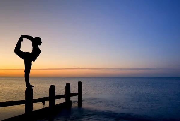 Silhouette of woman stretching doing yoga on groynes on beach — Stock Photo, Image