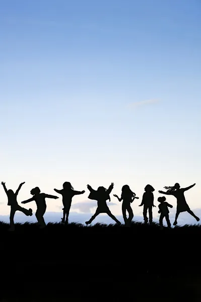 Silhhouette of group of kids playing around and jumping against — Stock Photo, Image