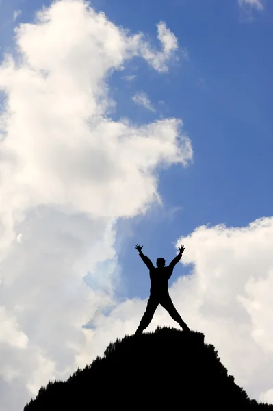 Silhouette of man on top of peak stretching arms towards sky in — Stock Photo, Image