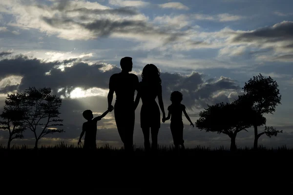 Silueta de familia joven caminando a través de campos y árboles — Foto de Stock